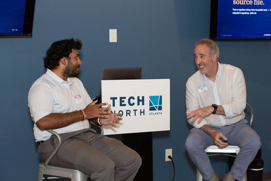 Mike and Sreyas Gentela seated facing each other, laughing, with the “Your story is your source file” slide behind them.